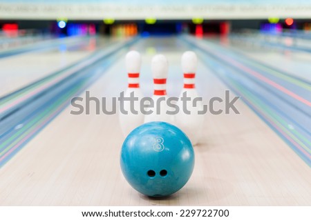 Bowling game. Close-up of blue bowling ball lying against pins staying on bowling alley