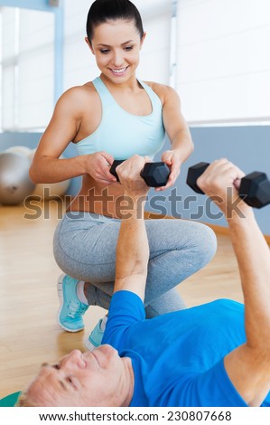 Supporting in every move. Confident female physical therapist supporting senior man in weight exercises