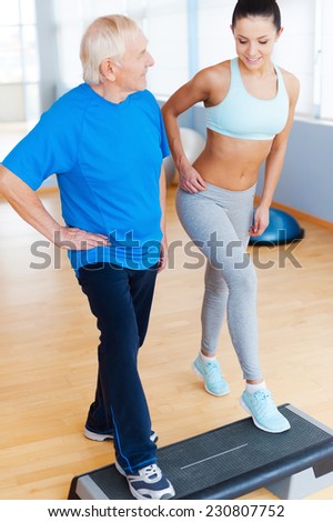 Do it this way. Full length of cheerful physical therapist working with senior man in health club