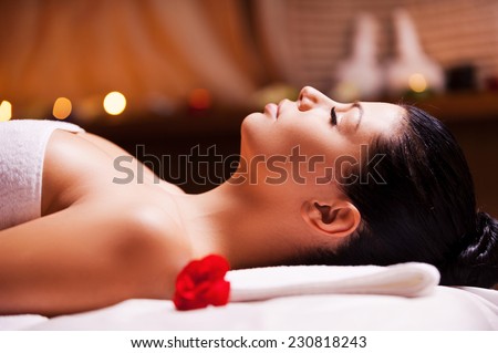 Total relaxation. Side view of beautiful young woman wrapped in towel lying on massage table and keeping eyes close