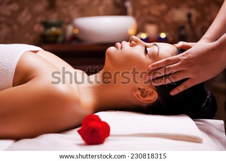 Stress removing. Side view of beautiful young woman lying on back while massage therapist massaging her head