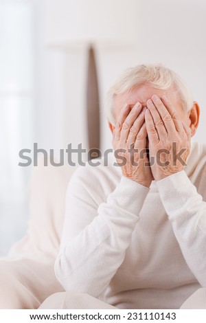 Loneliness. Frustrated senior man covering his face by hands while sitting in chair