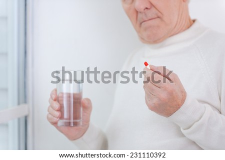 Taking care of his health. Cropped image of senior man holding medicines while standing near the window