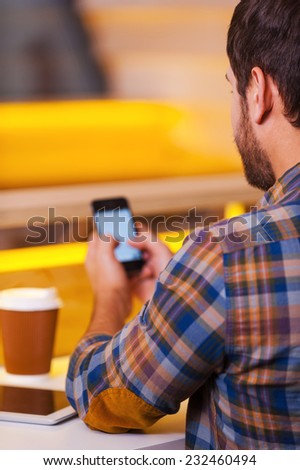 Texting message to friend. Rear view of man texting on his mobile while sitting in coffee shop