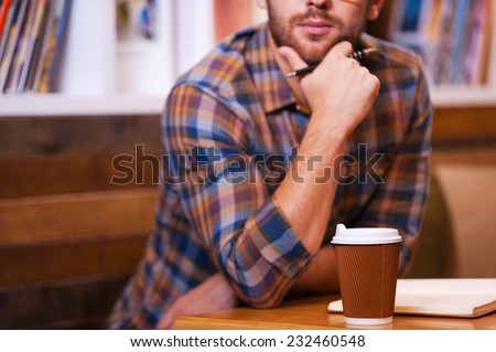 Lost in thoughts. Close-up of thoughtful young man holding hand on chin while sitting at the desk in library