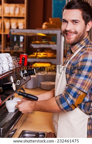 I love my job. Handsome male barista making coffee and smiling while standing at the bar counter near the coffee machine