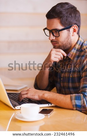 Inspire with cup of fresh coffee. Confident young man working on laptop while sitting in coffee shop