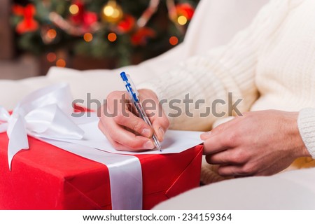 Christmas present. Close-up of man writing Christmas letter with Christmas Tree in the background