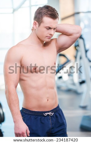 Feeling pain after workout. Frustrated young muscular man touching his neck and expressing negativity while standing in gym