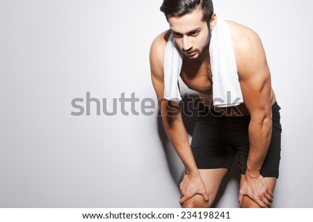 Feeling tired after workout. Young muscular man holding hands on his knees while standing against grey background