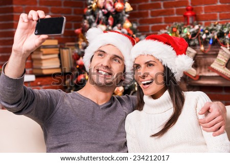 Capturing happy moments. Beautiful young loving couple bonding to each other and smiling while making selfie with Christmas Tree in the background