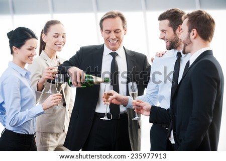 Celebrating success. Group of business people holding flutes with champagne and smiling while standing close to each other indoors