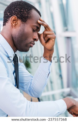 Hopeless and depressed. Side view of frustrated African man in shirt and tie touching his face and keeping eyes closed