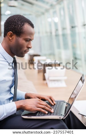 Businessman at work. Side view of young and confident African man in formalwear working on laptop while sitting at his working place