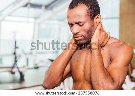 Feeling neckache after workout. Frustrated young African man touching his neck and expressing negativity while standing in gym