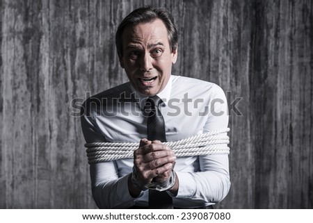 Fear and hopelessness. Shocked tied up businessman asking help while sitting at the chair with dirty wall  in the background