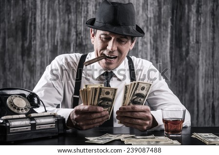 Money and power. Senior gangster in shirt and suspenders counting money and smiling while sitting at the table