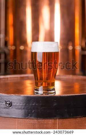 Fresh brewed lager. Close-up of glass with beer standing on the wooden barrel with metal container in the background