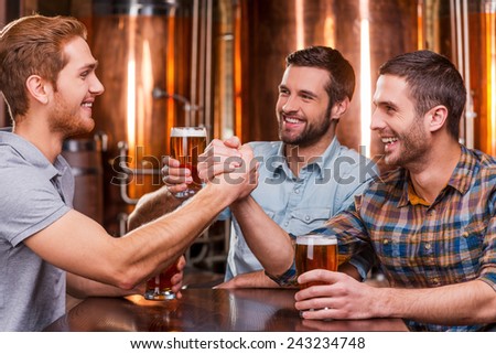 Spending great time with friends. Three happy young men in casual drinking beer while sitting in beer pub together