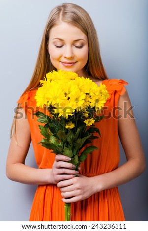 The most beautiful flowers for the most beautiful girl. Beautiful young woman in pretty dress holding bouquet of flowers while standing against grey background