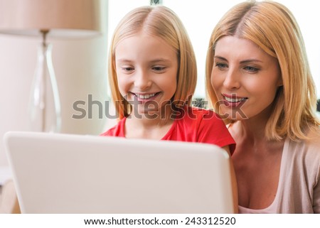 Surfing the net together. Happy mother and daughter bonding to each other and smiling while surfing the net together