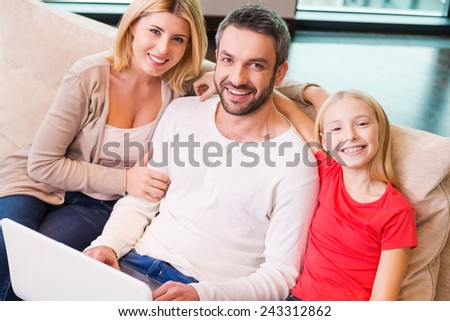 Family shopping online. Top view of happy family of three bonding to each other and smiling while surfing the net together at home