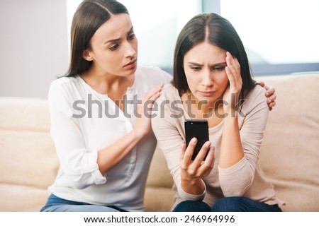 Real friends are always near. Depressed young woman holding mobile phone while being consoled by her friend