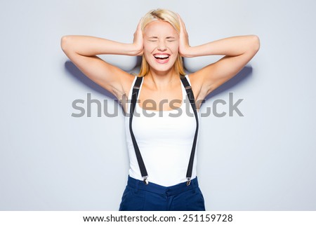 I refuse to hear you. Surprised young woman covering ears with hand and keeping eyes closed while standing against grey background