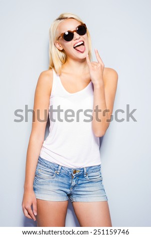 Rock and Roll queen. Beautiful young blond hair women making a face and gesturing while standing against grey background