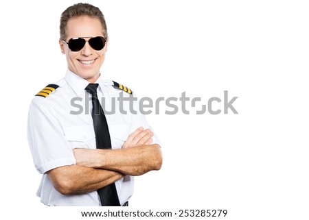 Confident pilot. Confident male pilot in uniform keeping arms crossed and smiling while standing against white background
