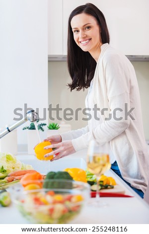 Only clean and fresh vegies for my salad. Beautiful young woman washing vegetables for salad and smiling while standing in the kitchen