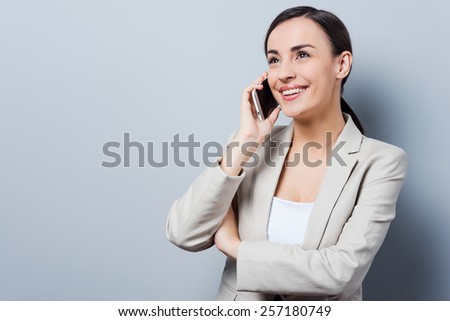 Conversation with pleasure. Beautiful young businesswomen talking on the mobile phone and smiling while standing against grey background