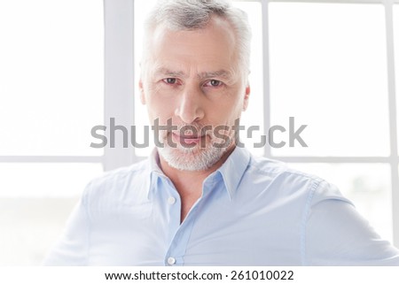 Confident and successful. Confident grey hair senior man in shirt looking ay camera while standing in front of the window