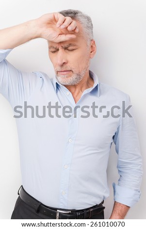 Feeling exhausted. Tired senior man in shirt touching head with hand and keeping eyes closed while standing against white background