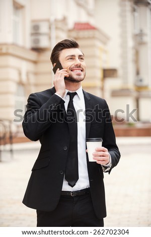Good business talk. Handsome young man in formalwear talking on the mobile phone and smiling while standing outdoors