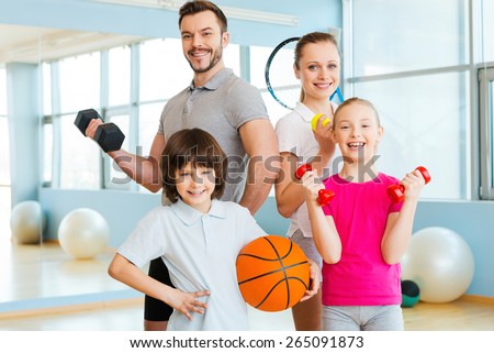 Happy and sporty. Happy family holding different sports equipment while standing close to each other in health club