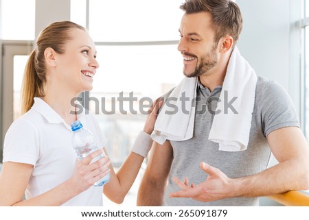 Meeting friends in sports club. Cheerful young man and woman talking to each other and smiling while both standing in sports club