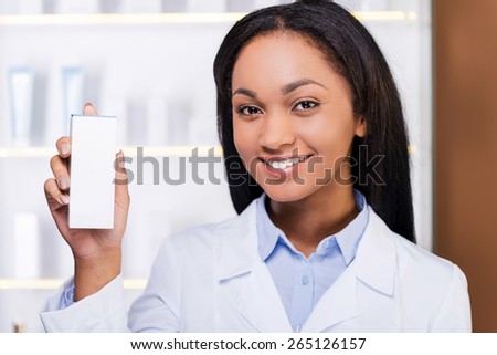 Professional advice. Beautiful young African woman in lab coat holding container with some medicine and smiling while standing in drugstore