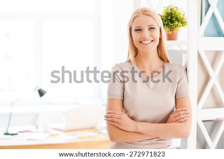 Cheerful businesswoman. Beautiful young woman leaning at the shelf and smiling while standing near her working place in office