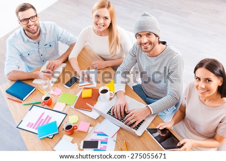 Creative team t work. Top view of group of business people in smart casual wear working together and smiling while sitting at the wooden desk