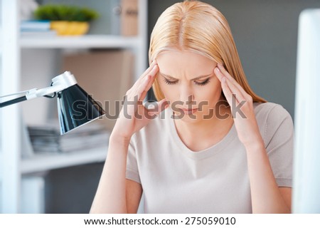 Feeling stressed. Frustrated young woman touching her head and keeping eyes closed while sitting at her working place in office