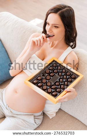 When the craving calls... Top view of beautiful pregnant young woman eating chocolates while sitting on sofa
