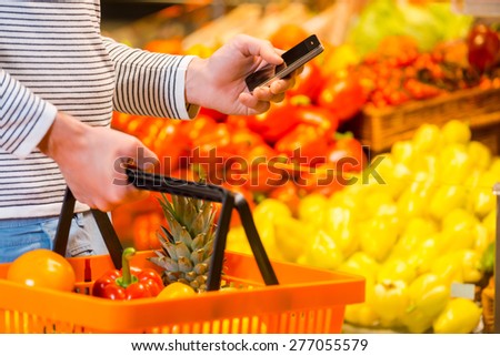 Trying not to forget to buy everything. Close-up of young men holding shopping bag and mobile phone while standing in a food store