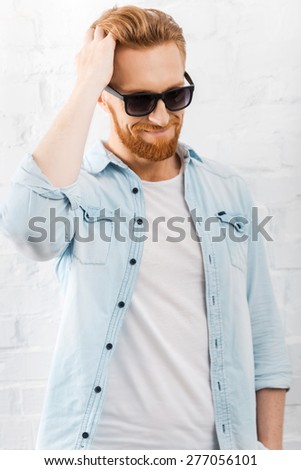 Hairstyle for fashion style. Handsome young bearded man holding hand in hair and smiling while standing against brick wall