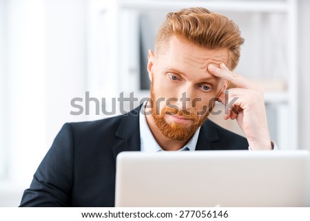 Some business troubles. Frustrated bearded businessman working on laptop and touching his head while sitting at his working place