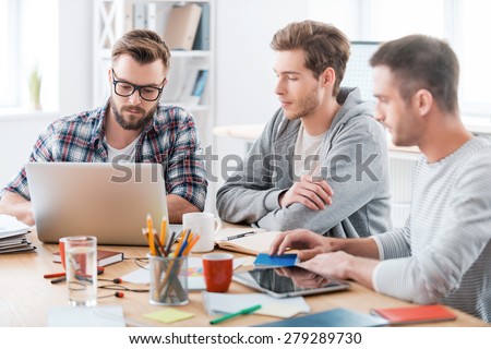 Together they will figure it out. Three young confident men working together while sitting at their working place in office