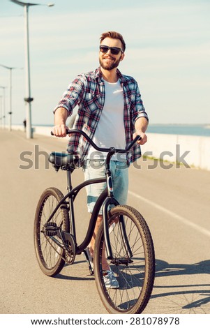 Time for a cycle. Handsome young smiling man walking along a road with his bicycle