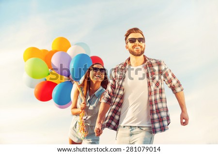 Living life to the fullest. Cheerful young couple holding hands and smiling while walking outdoors with colorful balloons