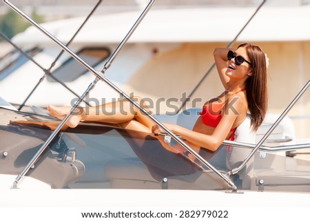 Beauty on yacht. Happy young woman holding hand in hair and smiling while sitting on the board of yacht