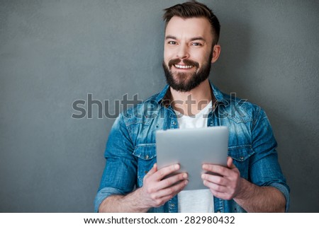 Smart technology makes everything easier. Happy young man holding digital tablet and smiling at camera while standing against grey background